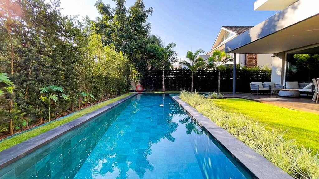 Vista da piscina retangular cercada por vegetação em casa moderna com área verde em Jurerê Internacional